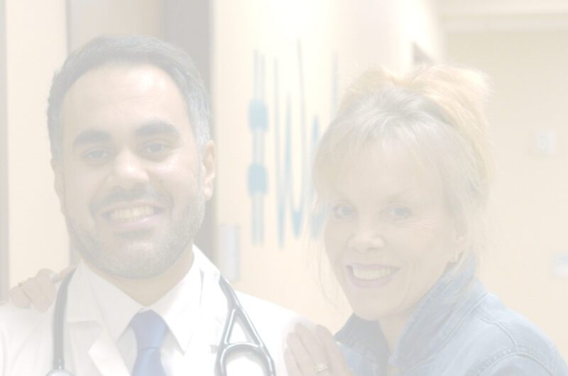 A doctor with a stethoscope around his neck stands next to a smiling woman in an RP clinic hallway, both looking at the camera. The image is faded and softly lit.