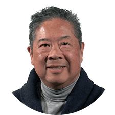 Smiling middle-aged man with short, gray hair wearing a gray turtleneck and dark jacket, against a plain white background.
