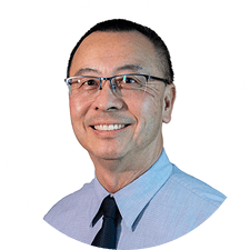 Smiling man with short dark hair and glasses, wearing a light blue button-up shirt and dark tie, stands against a plain white background—an approachable professional, representative of Matrix Radiologists.