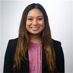 A woman with long brown hair, wearing a black blazer over a pink blouse, smiles at the camera in a professional setting focused on mammography and AI.