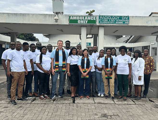 group of about 20 people, men and women, are posing and smiling together outside a hospital