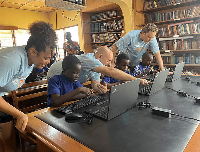 children being taught how to use computers in a classrooms by adult mentors