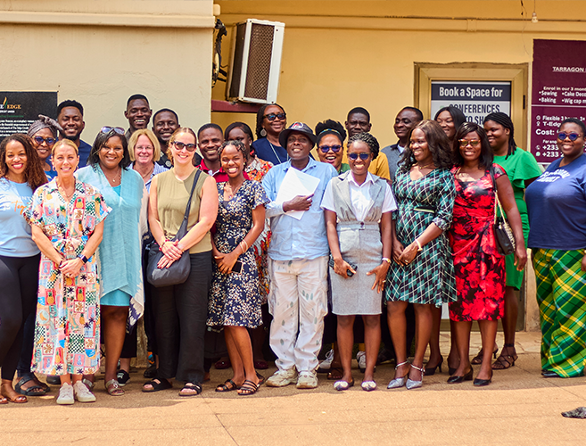group of about 20 people, men and women, are posing and smiling together outside a school